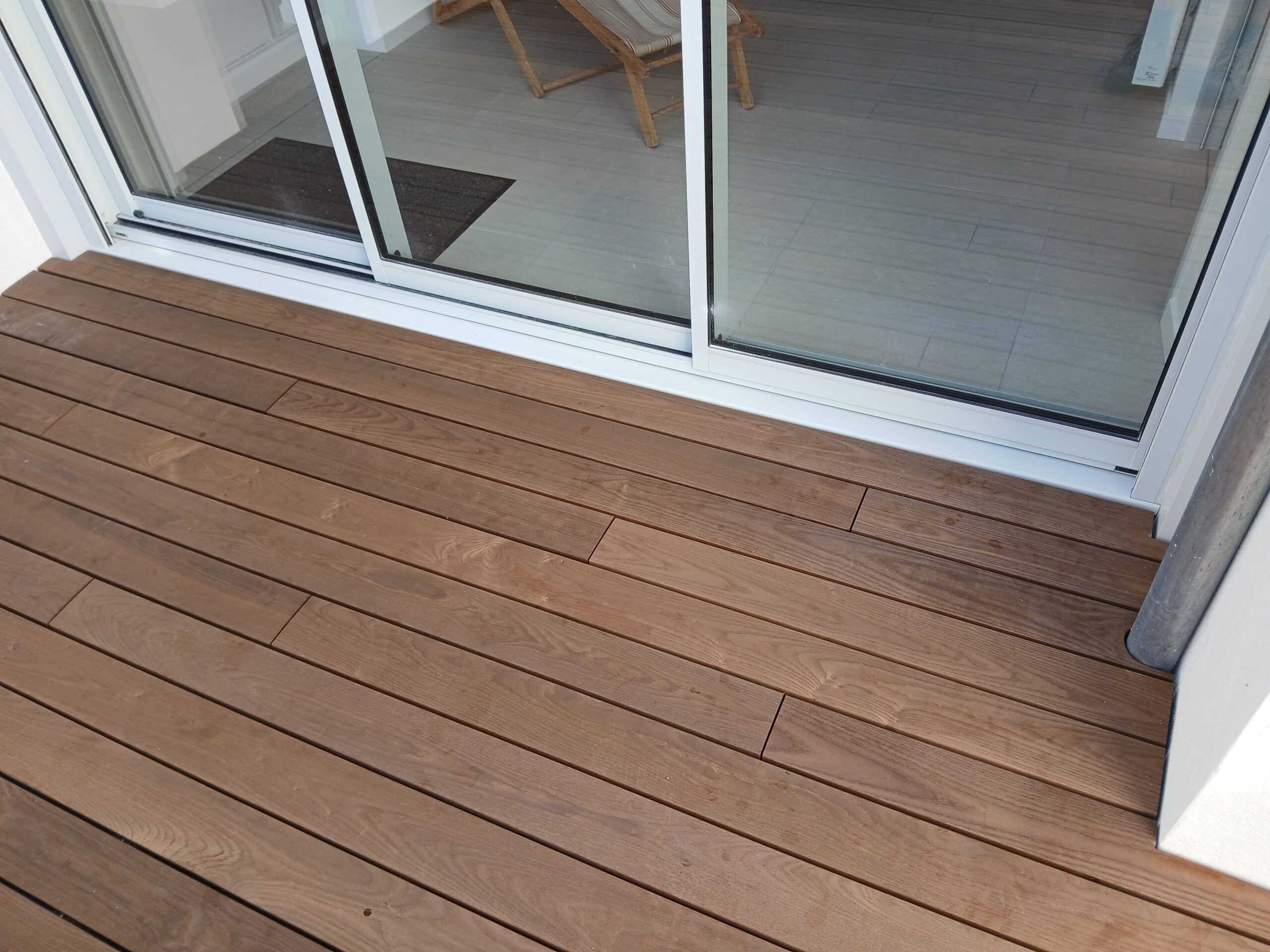 Terrasse en lames de bois brun devant une baie vitrée coulissante. Aménagement extérieur moderne et épuré.