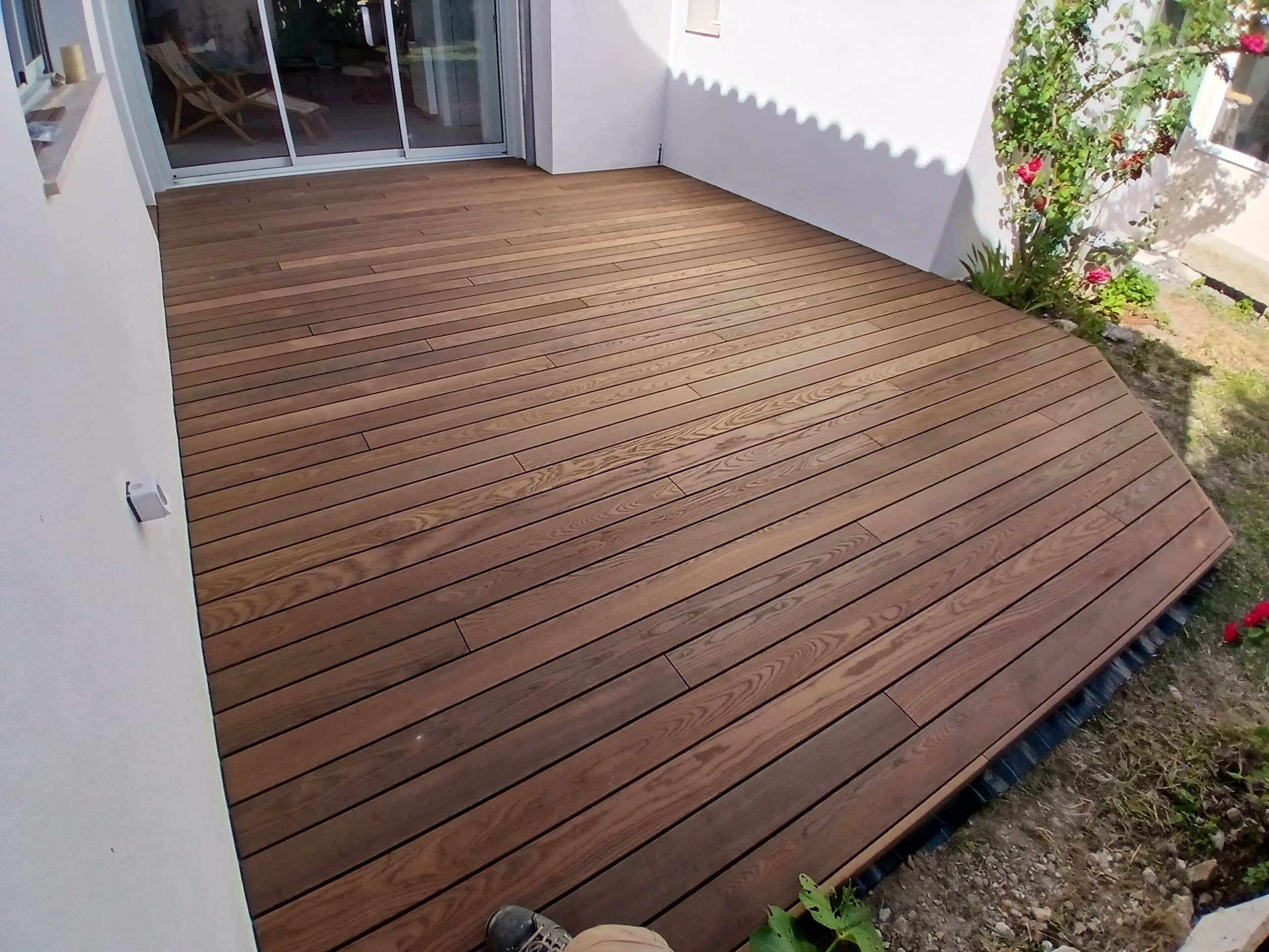 Terrasse en bois traité brun foncé aux lames régulières installée devant une maison moderne.