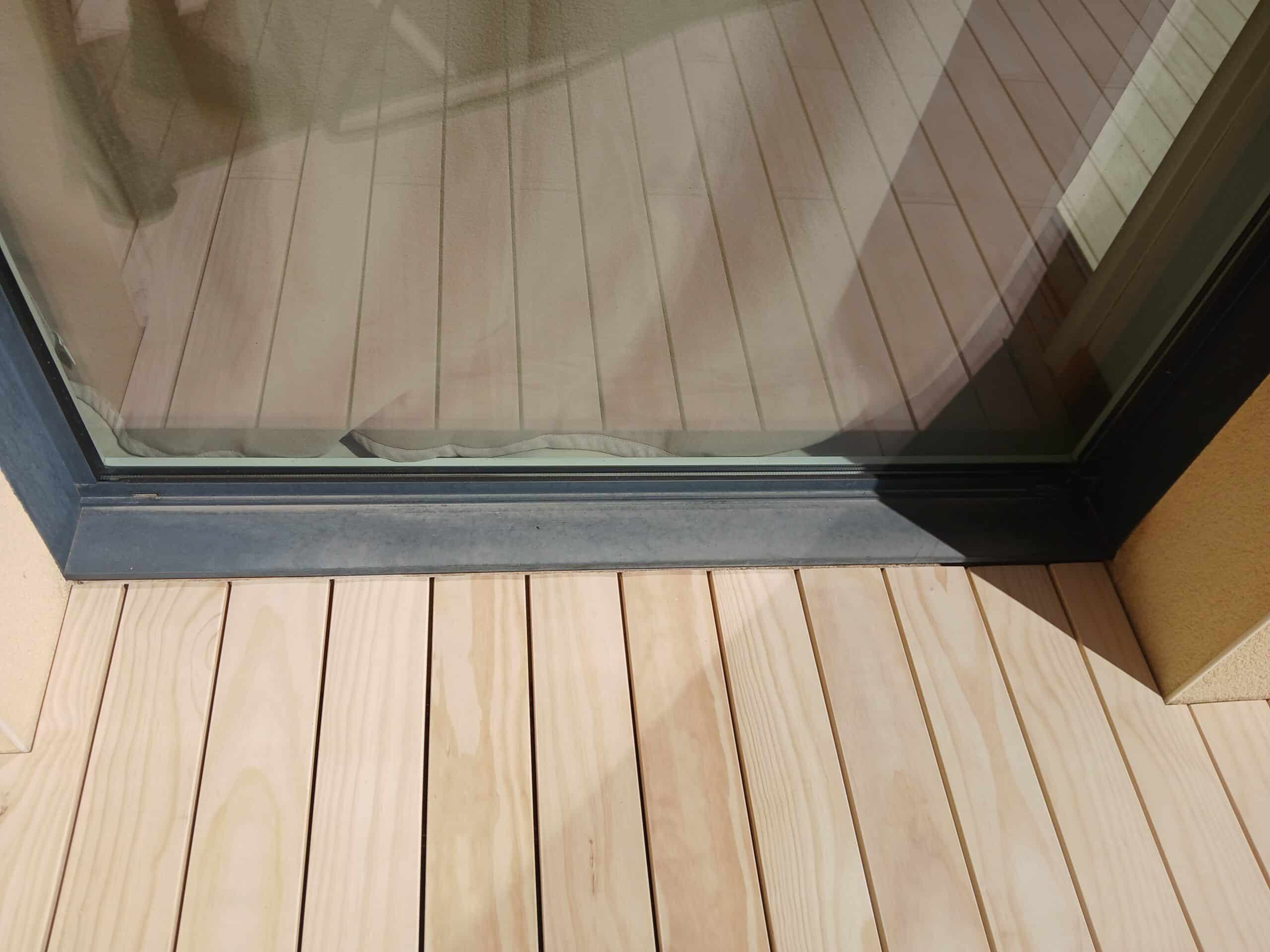 Lames de terrasse en bois clair longeant une baie vitrée au cadre anthracite moderne.