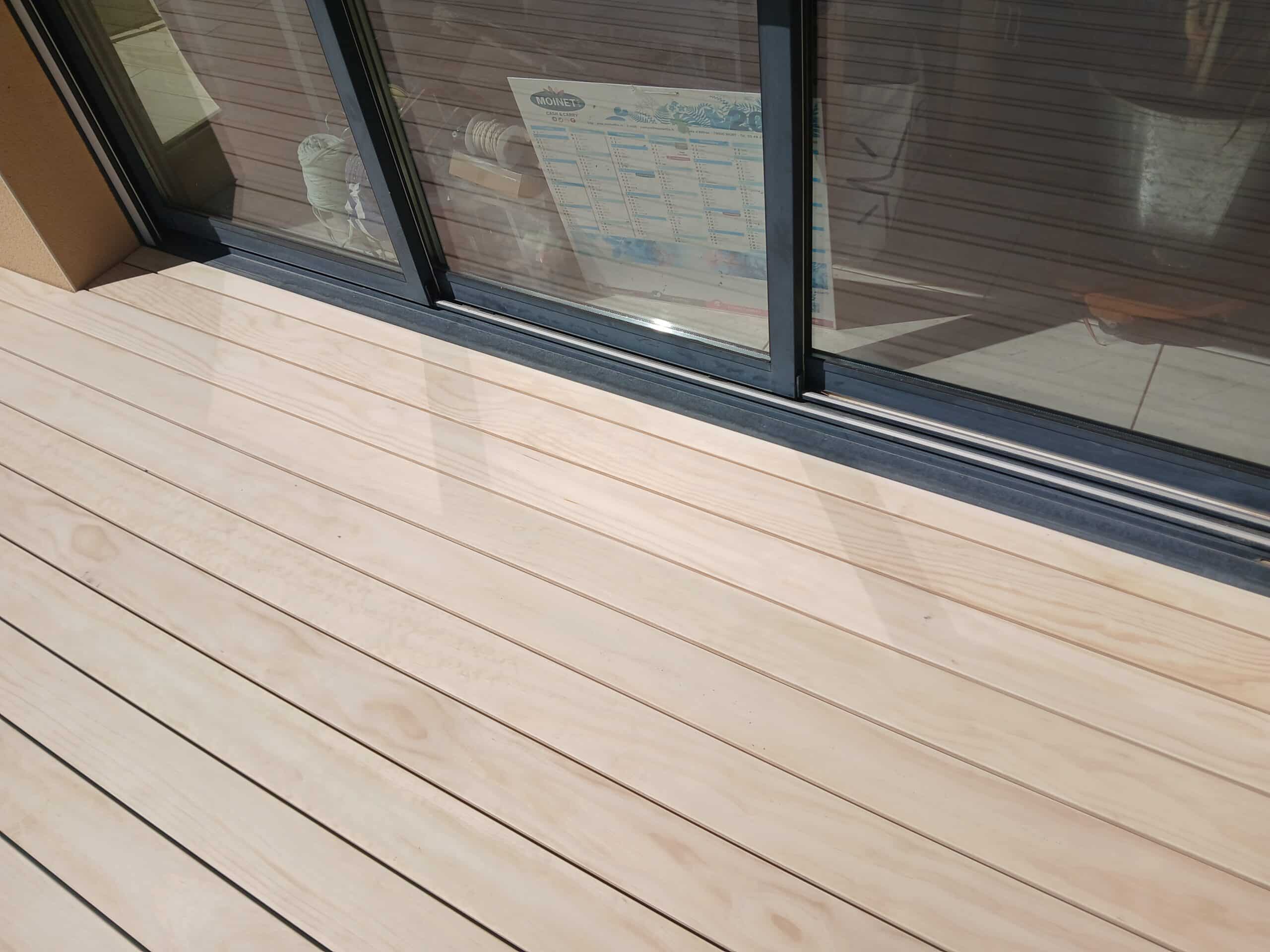 Terrasse bois clair et baie vitrée alu noir avec reflet calendrier Moinet.
