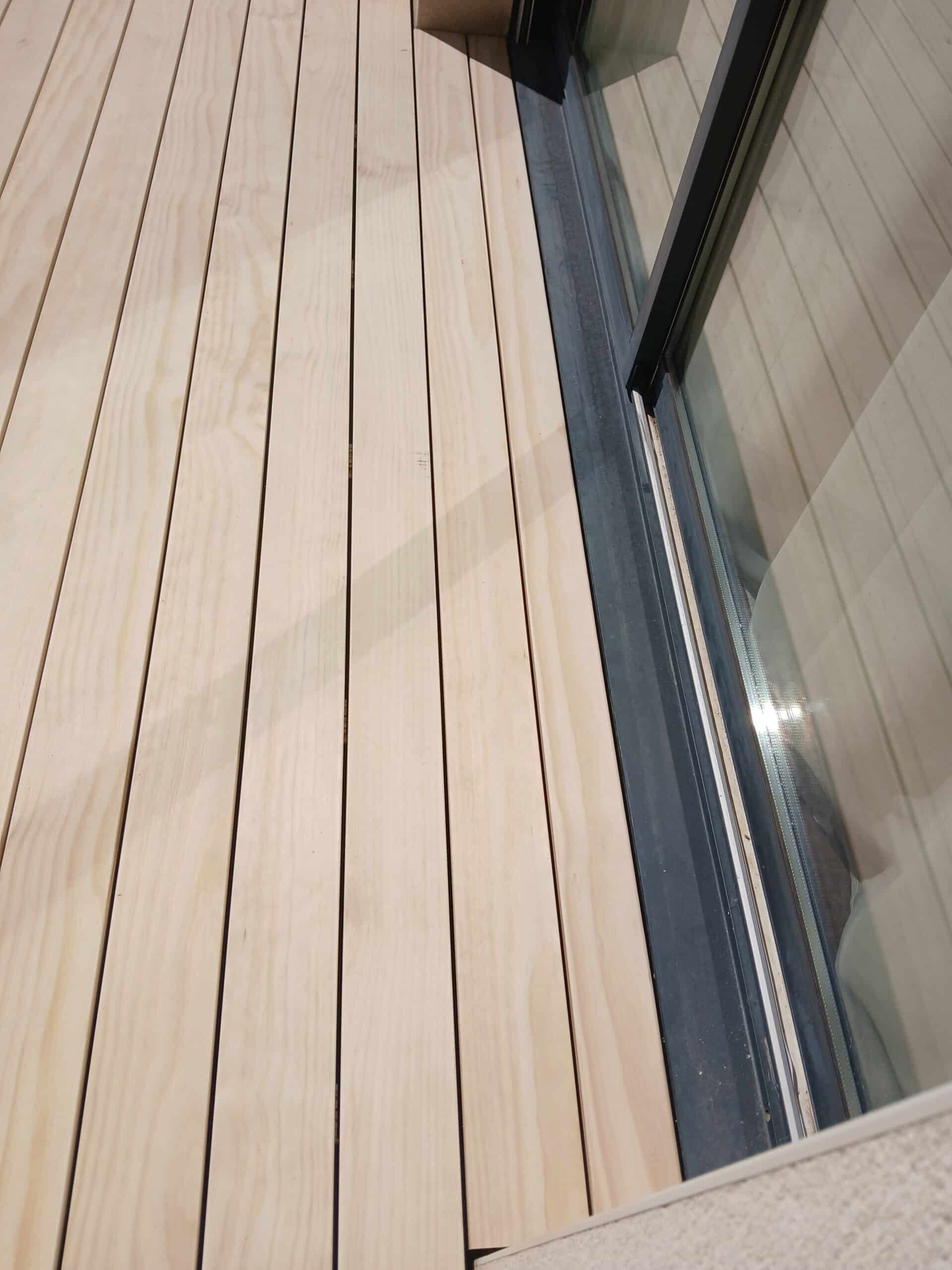 Terrasse en bois clair bordant un châssis de baie vitrée coulissante gris foncé.